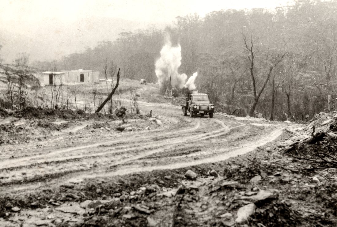 Huntley Colliery access road under construction, with a vehicle and blasting smoke